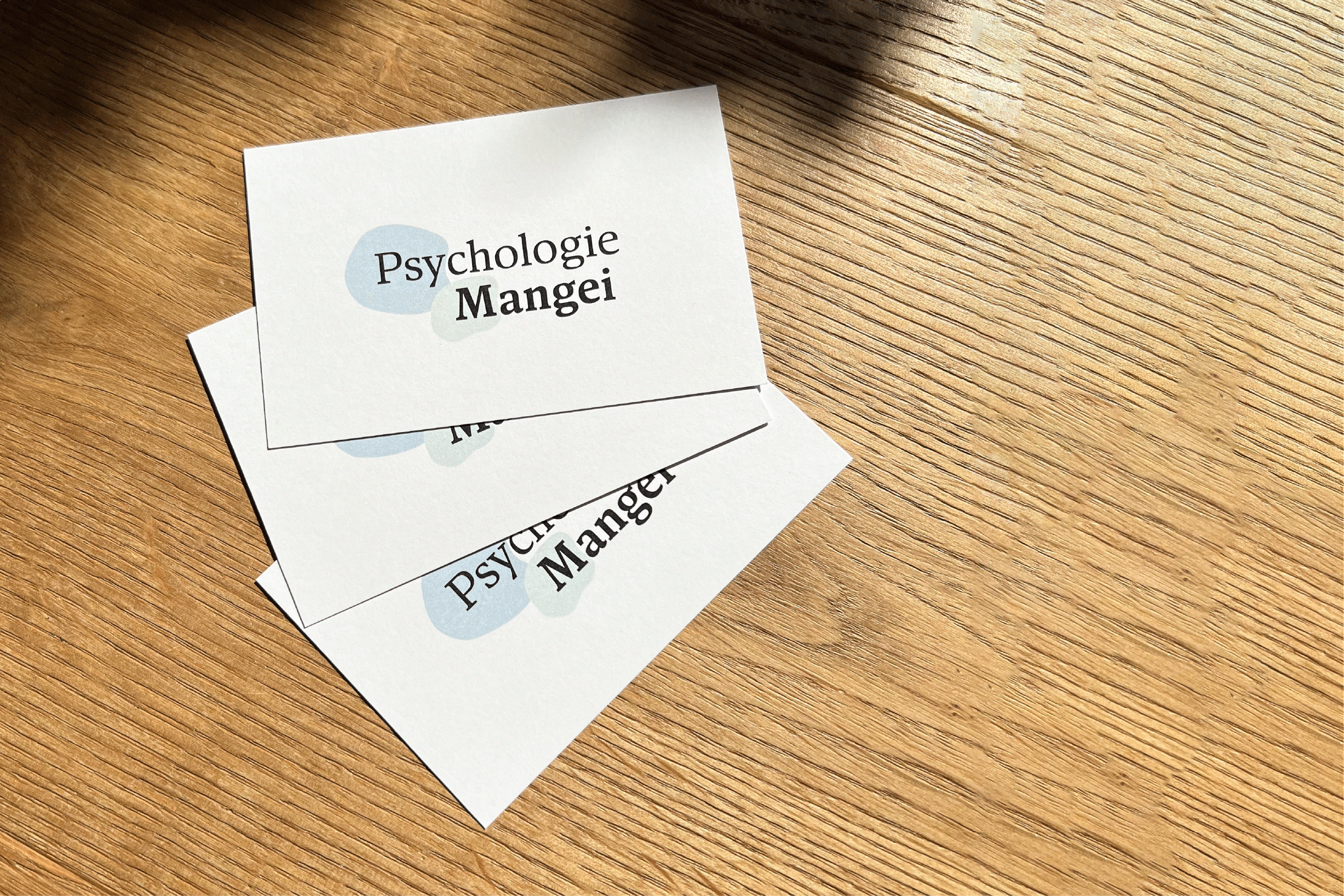 Drei Visitenkarten mit dem Logo Psychologie Mangei auf einem Holztisch arrangiert