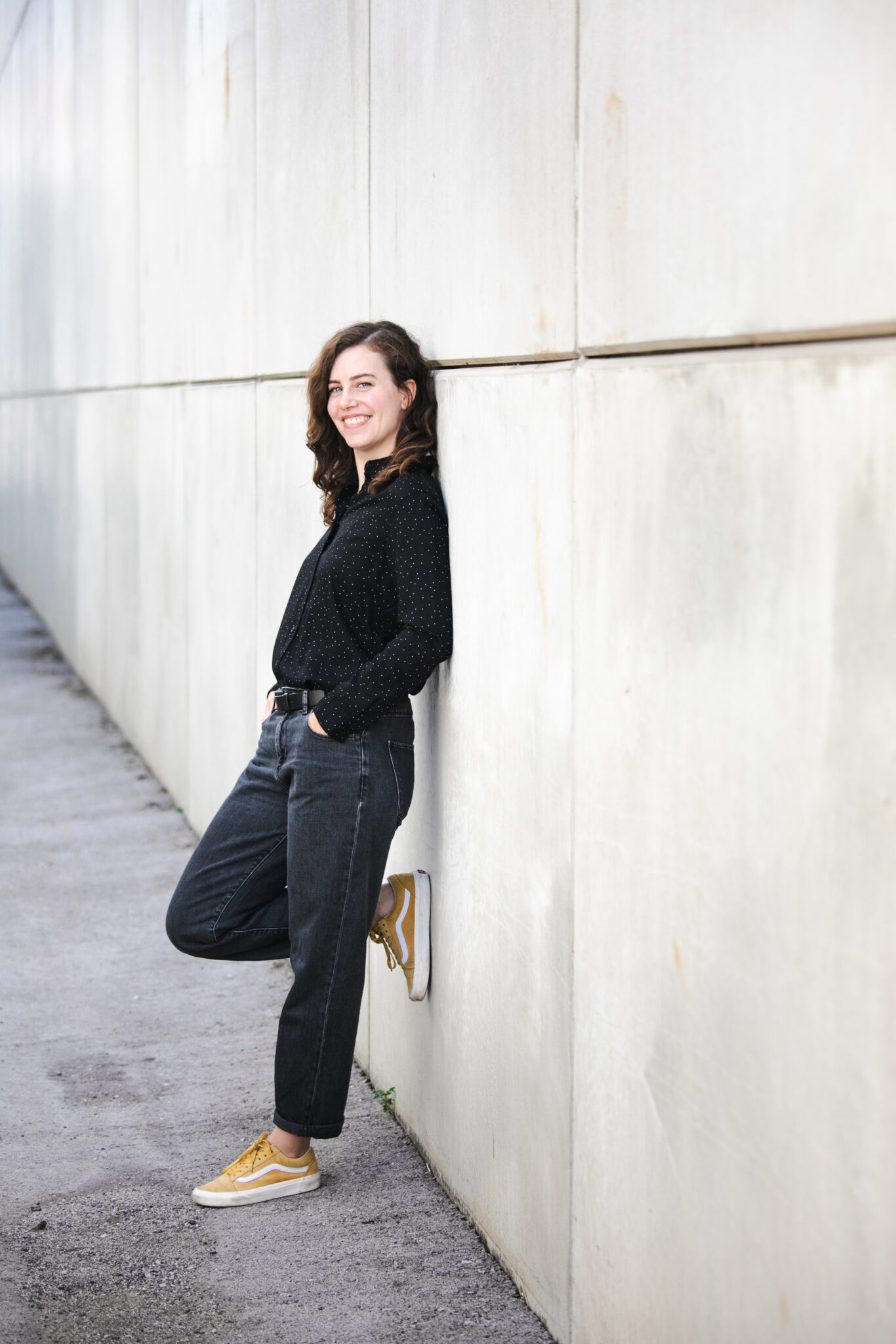 Stefanie Dippelreiter, Brand Designerin aus Wien, lehnt lässig an einer hellen Betonwand – Porträt für Impact with Love · Brand Design