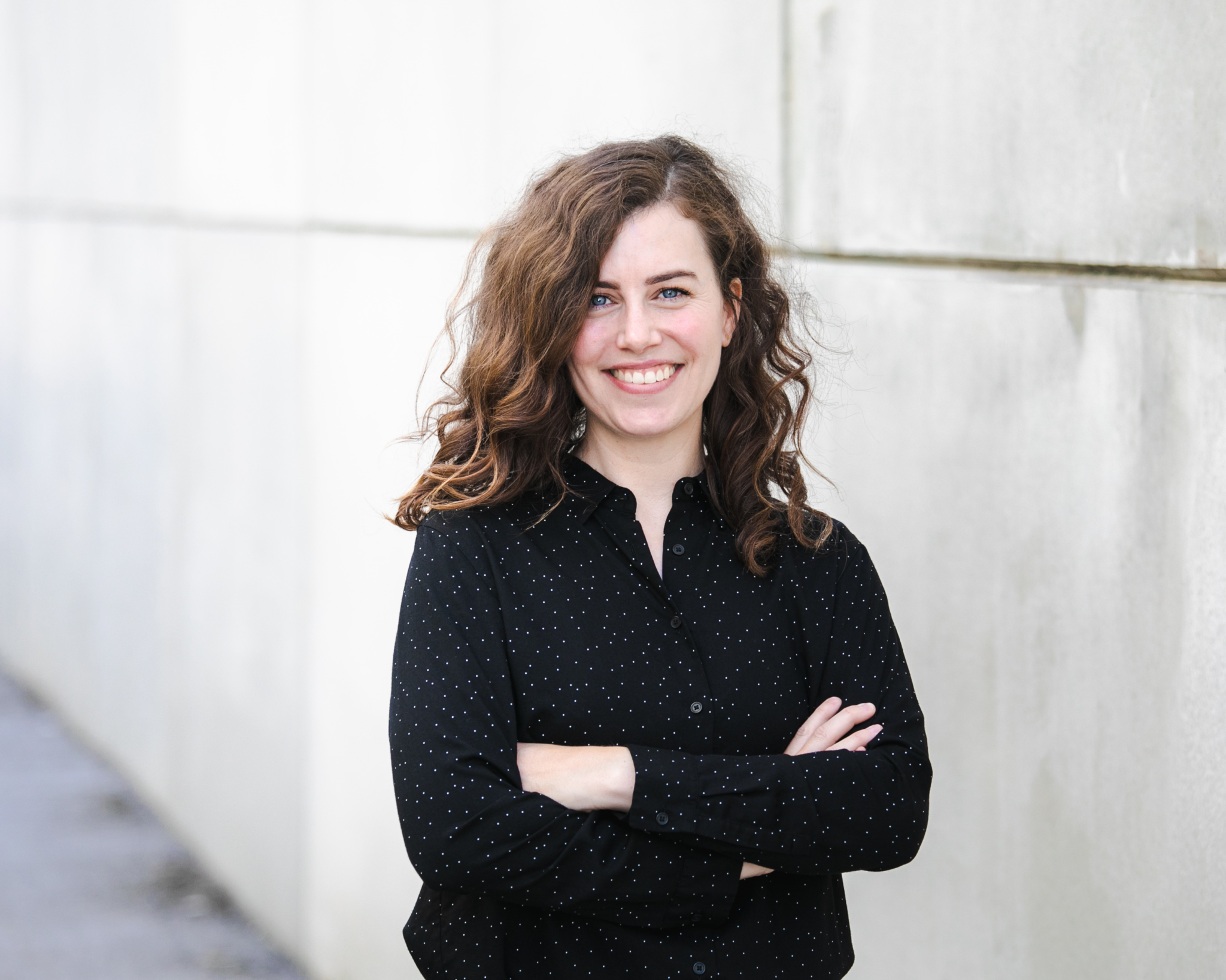 Stefanie Dippelreiter, Senior Brand Designerin, steht mit verschränkten Armen vor einer hellen Wand – authentisches Porträt für Impact with Love · Brand Design