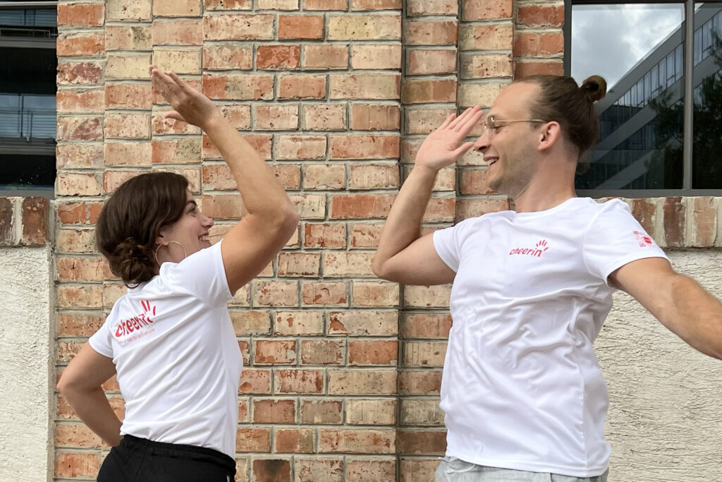 cheerin' Founder Manu & cheerin' Brand Designer Stef doing a high five while jumping while wearing our cheerin' brand t-shirts.